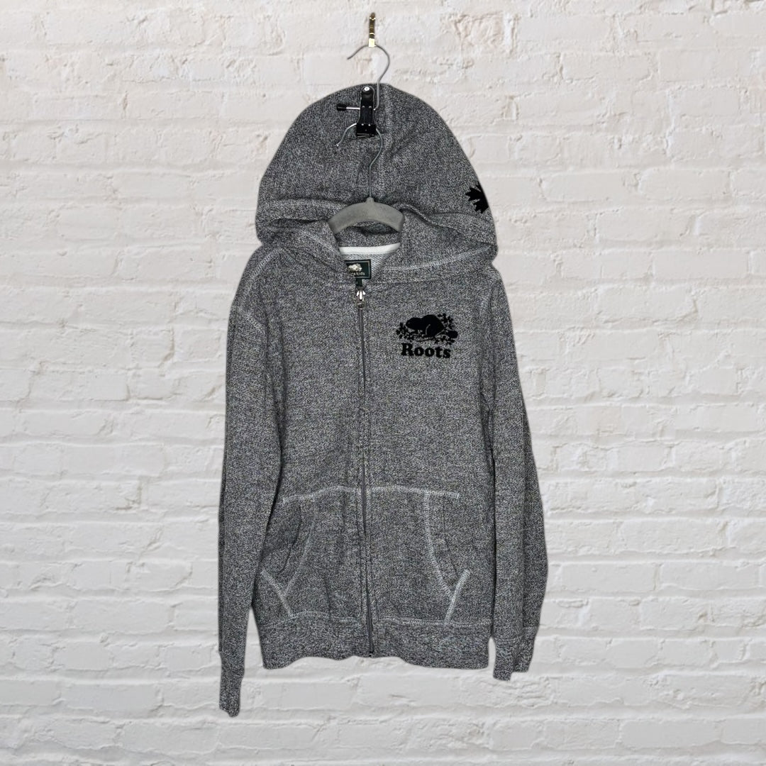 Grey Roots full-zip hoodie with logo, hanging on a brick wall.