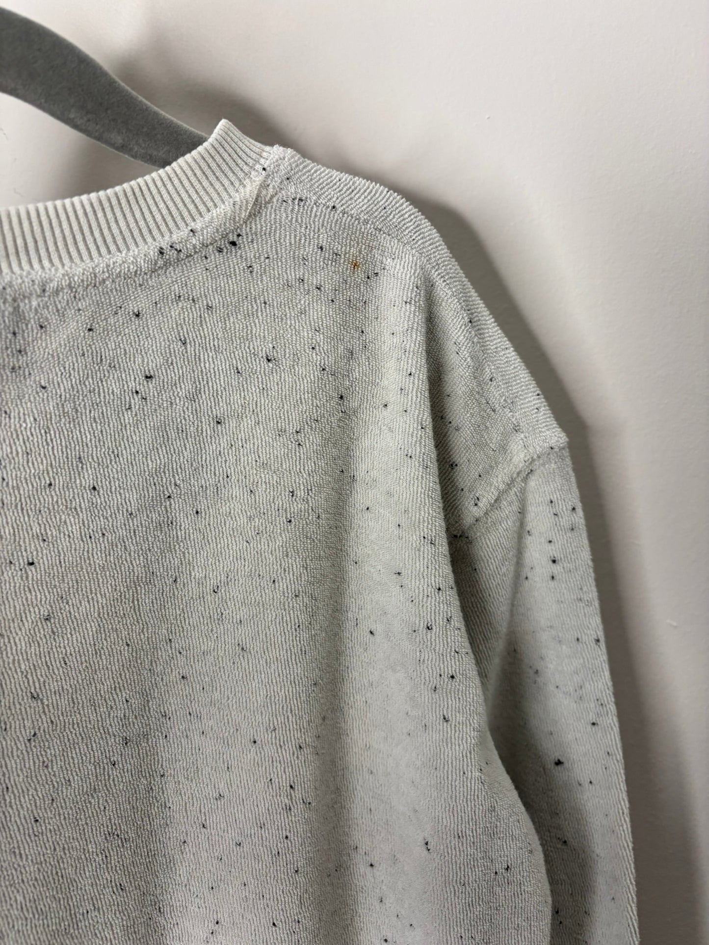 Light grey speckled sweatshirt with 'Imperfectly Perfect' text on the chest, displayed on a hanger against a brick wall.