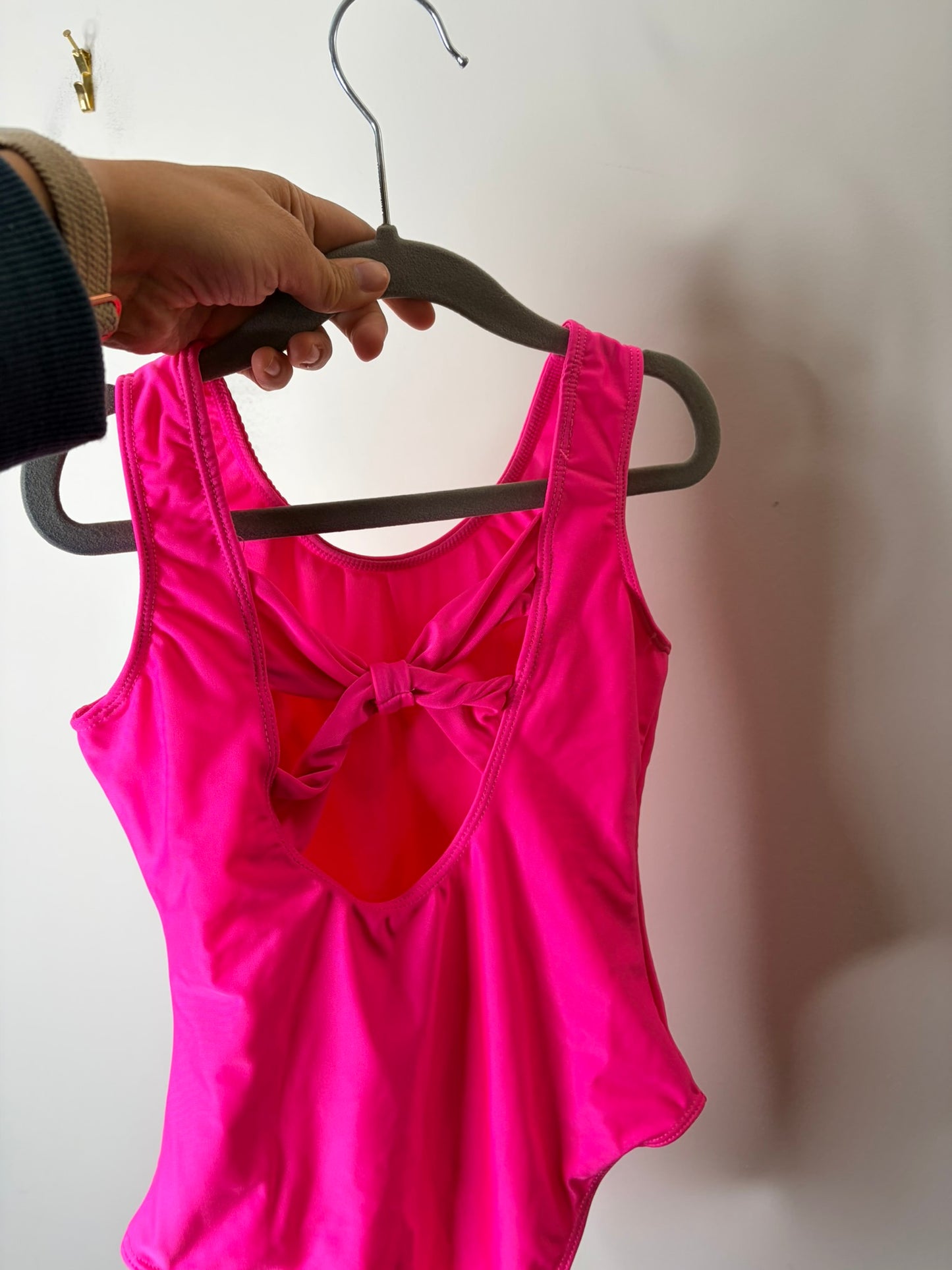 Neon pink bodysuit with silver 'Barbie' logo on the front, displayed on a hanger.