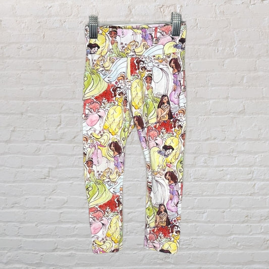 Multicolored leggings featuring various Disney princess characters, displayed against a white brick wall.