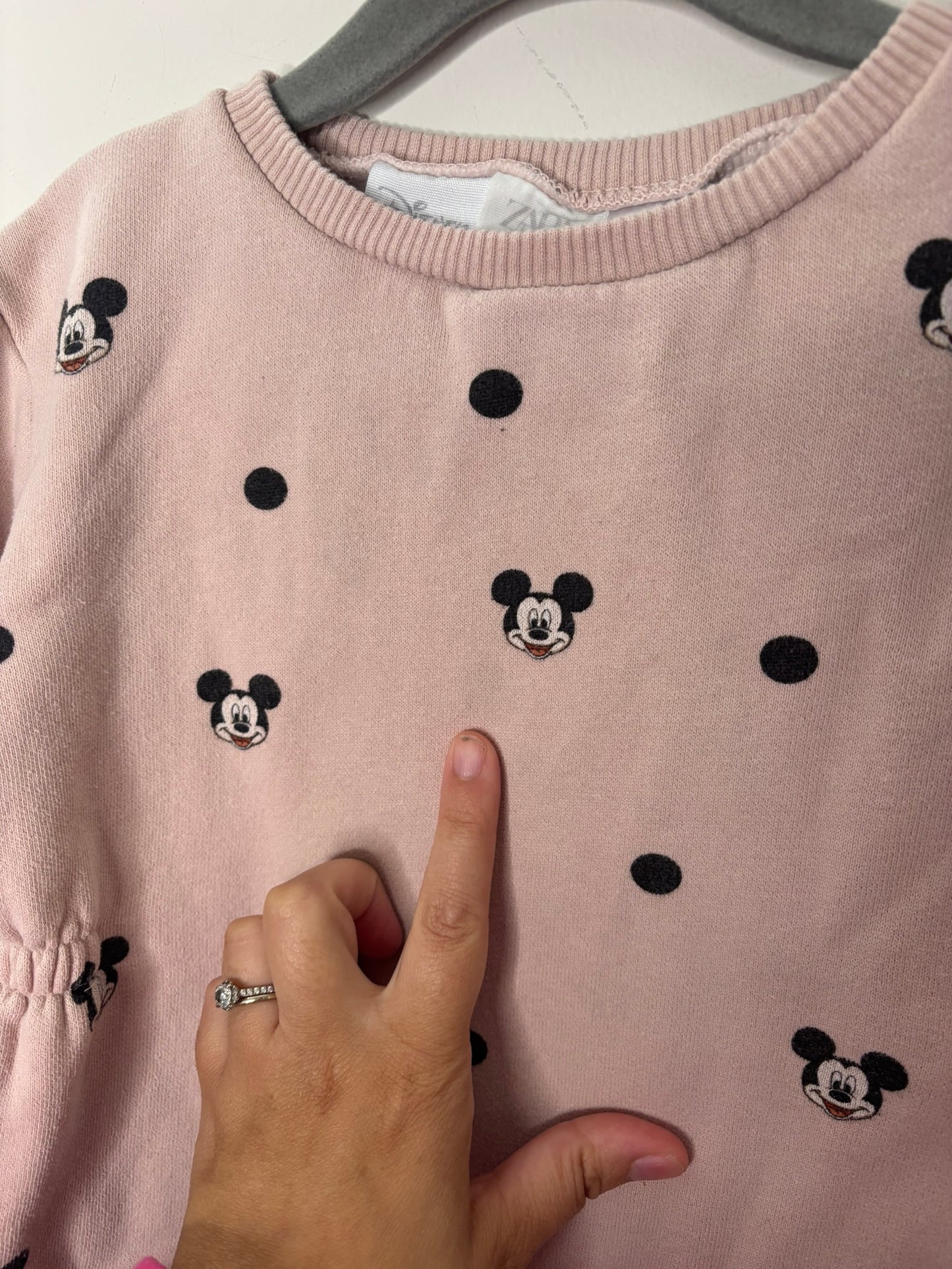 Pink sweatshirt dress with black Mickey Mouse and polka dot print, hanging on a hanger.