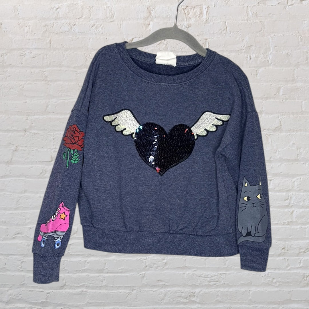Navy sweatshirt with a sequin heart and wings design, featuring colorful patchwork including a rose, roller skate, and a cat.