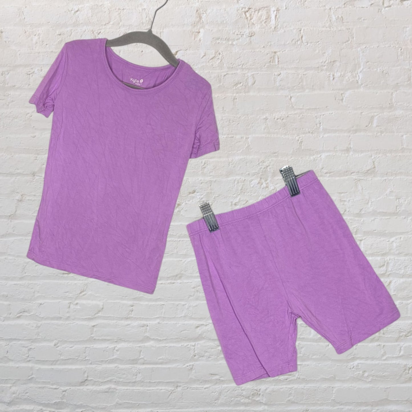 Purple short-sleeve top and shorts sleepwear set from Kyte, displayed against a white brick wall.