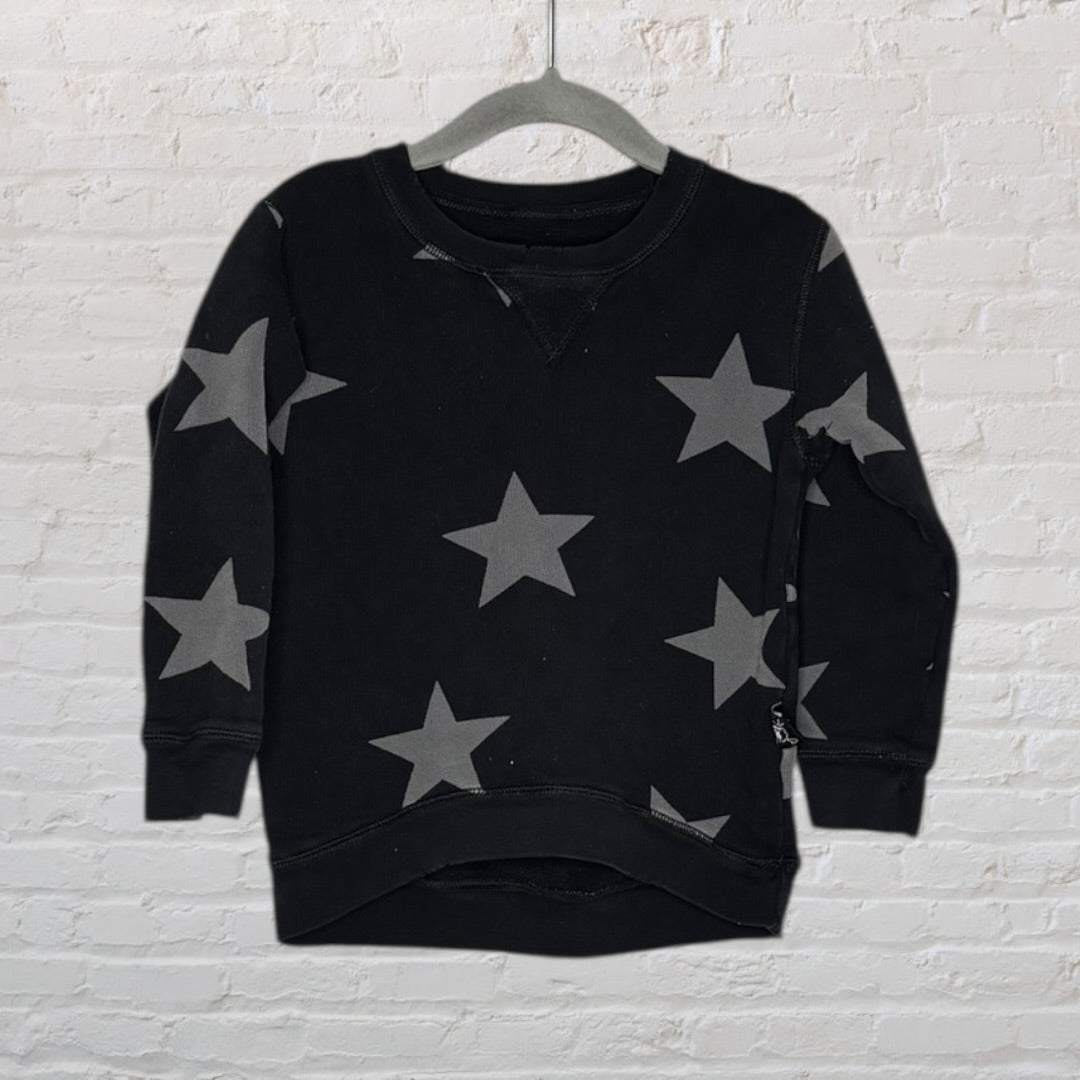 Black sweatshirt with grey star patterns displayed on a hanger against a white brick wall.