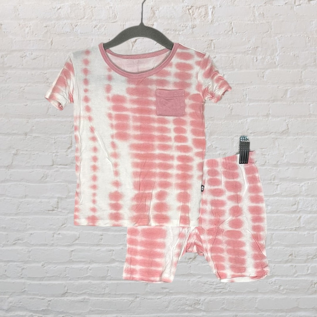 Pink and white tie-dye pajama set with short sleeves and a pocket, hanging against a white brick wall.