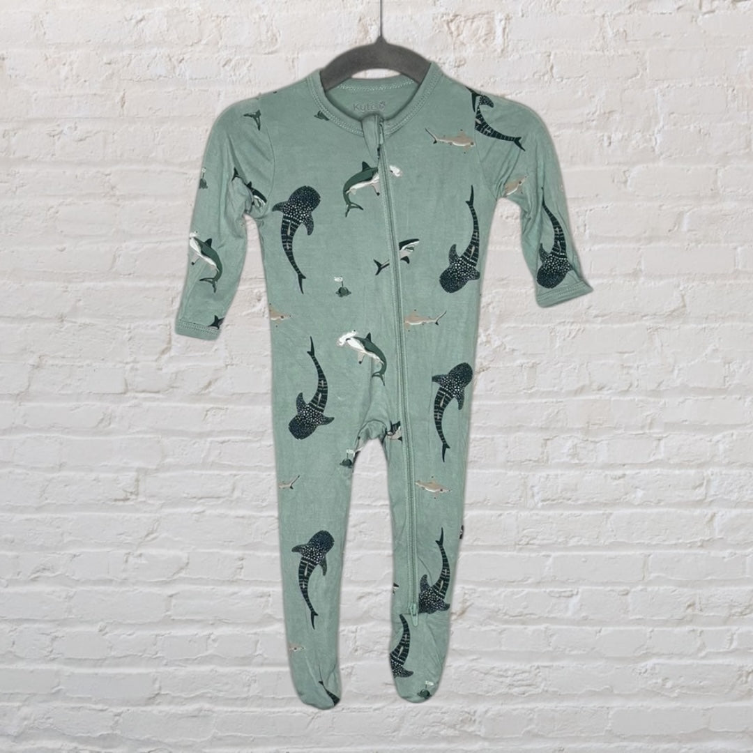 Seafoam green baby onepiece pajama with shark print, hanging on a hanger against a white brick wall.