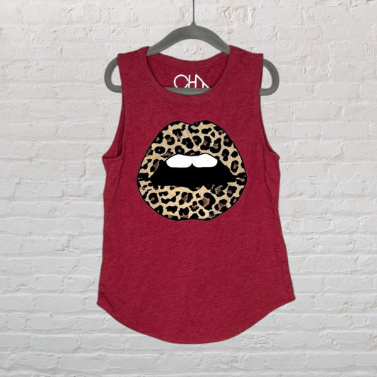 Red tank top with a leopard print lip graphic hanging on a hanger against a white brick wall.
