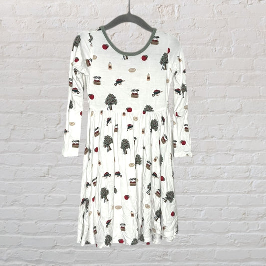 White long sleeve dress with various patterns including trees, apples, and houses, hanging on a hanger.