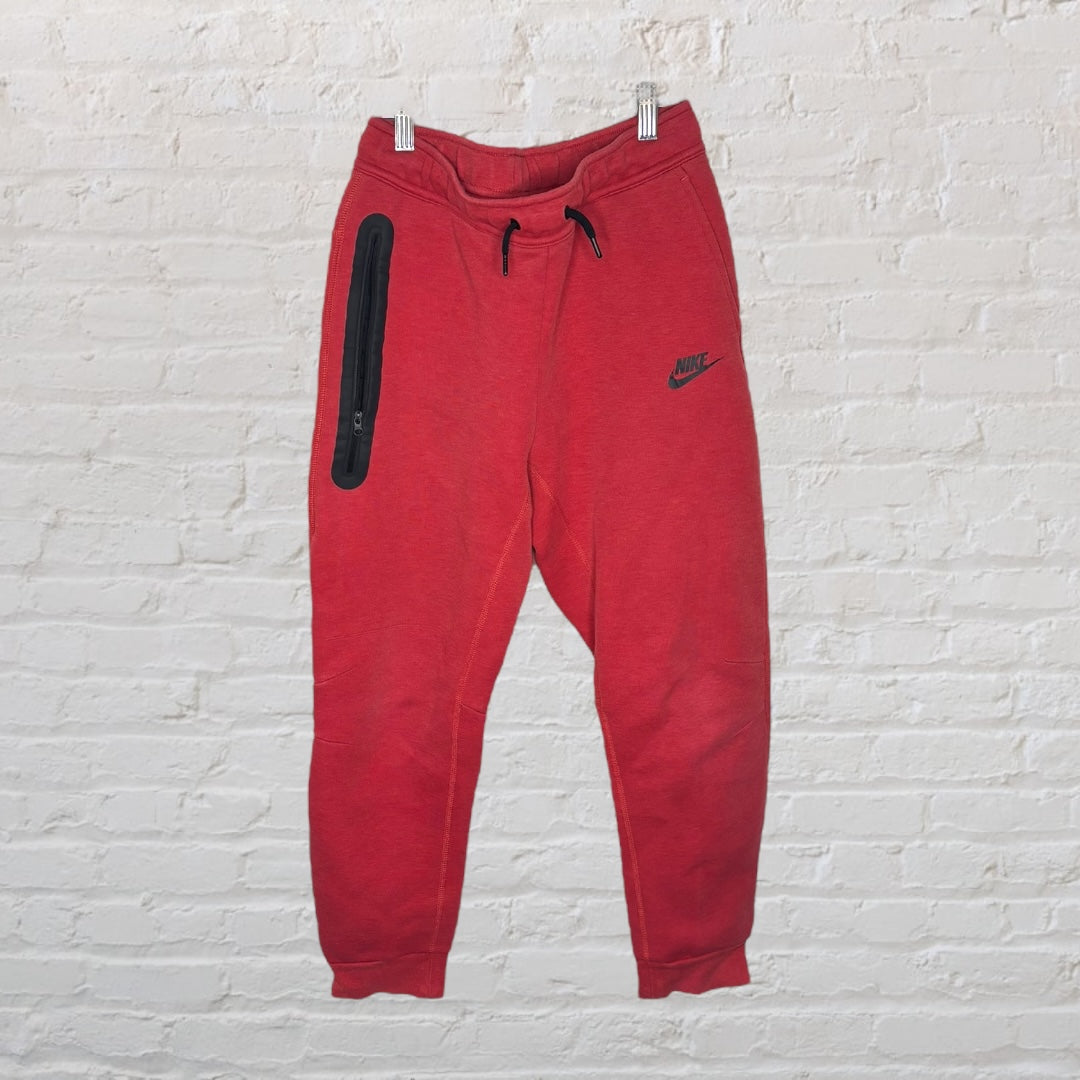Red Nike full-zip hoodie and sweatpants set with black accents, displayed on a white brick wall.
