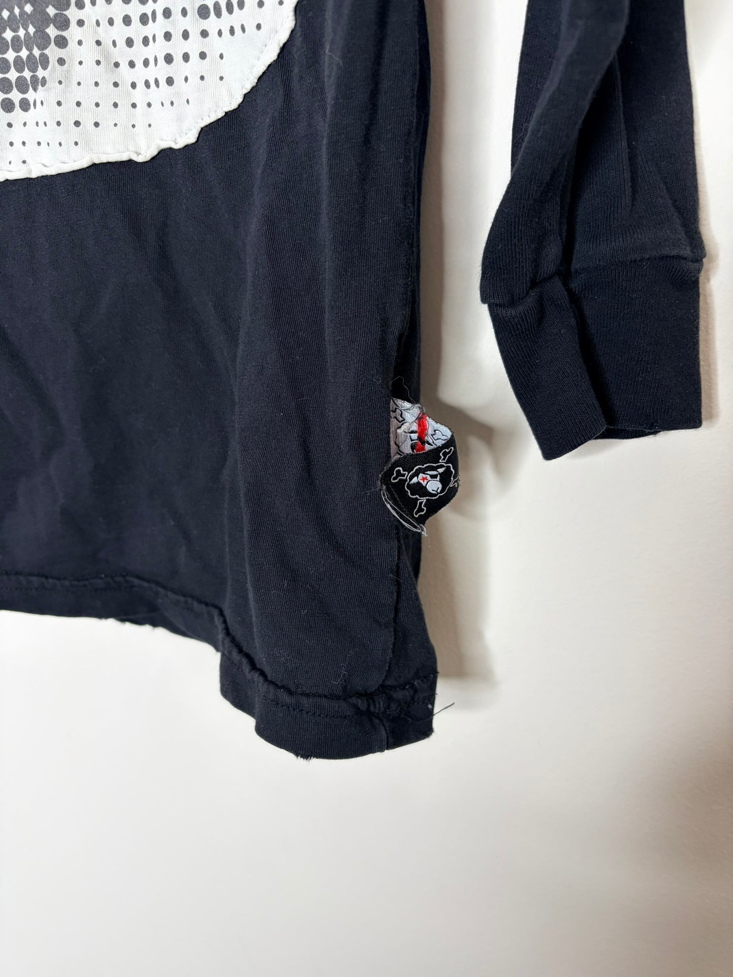 Black long sleeve t-shirt with a large white graphic eye design on the front, hanging against a brick wall backdrop.