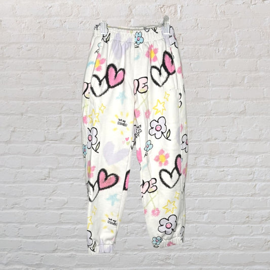 White sweatpants with colorful graphic prints of hearts, flowers, and stars.