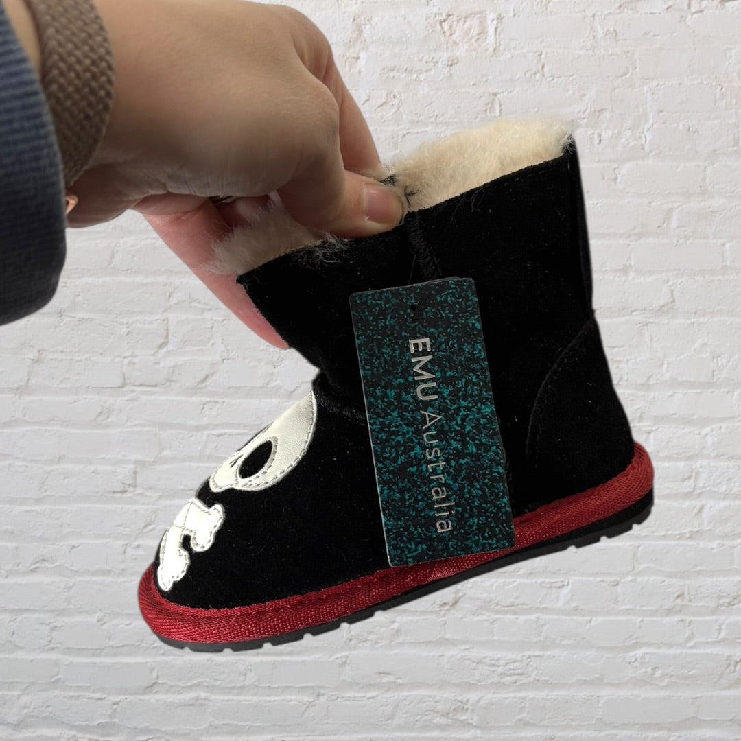 Pair of black shearling boots with white skull and crossbones design and red soles.