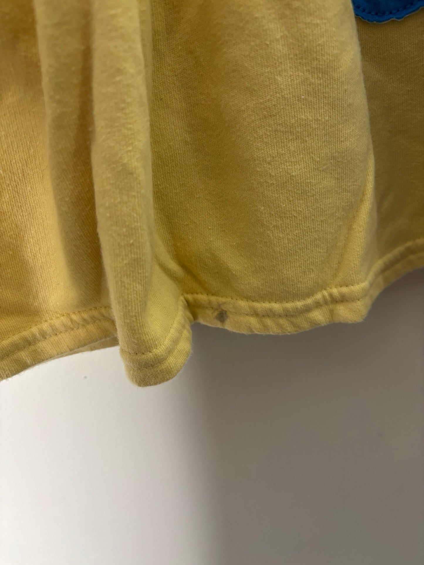 Yellow long sleeve dress with a colorful flower patch on the lower front, hung on a hanger against a white brick wall.