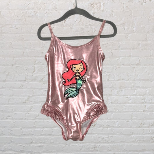 Shiny pink swimsuit with mermaid graphic and ruffle details on the bottom, hanging on a black hanger.
