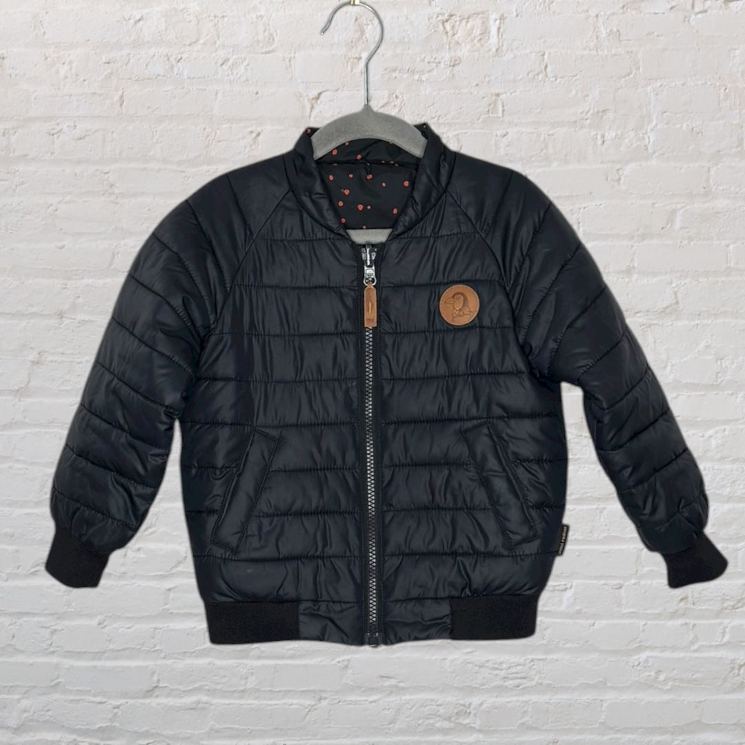 Black puffer jacket with red polka dots, hung on a hanger against a white brick wall.
