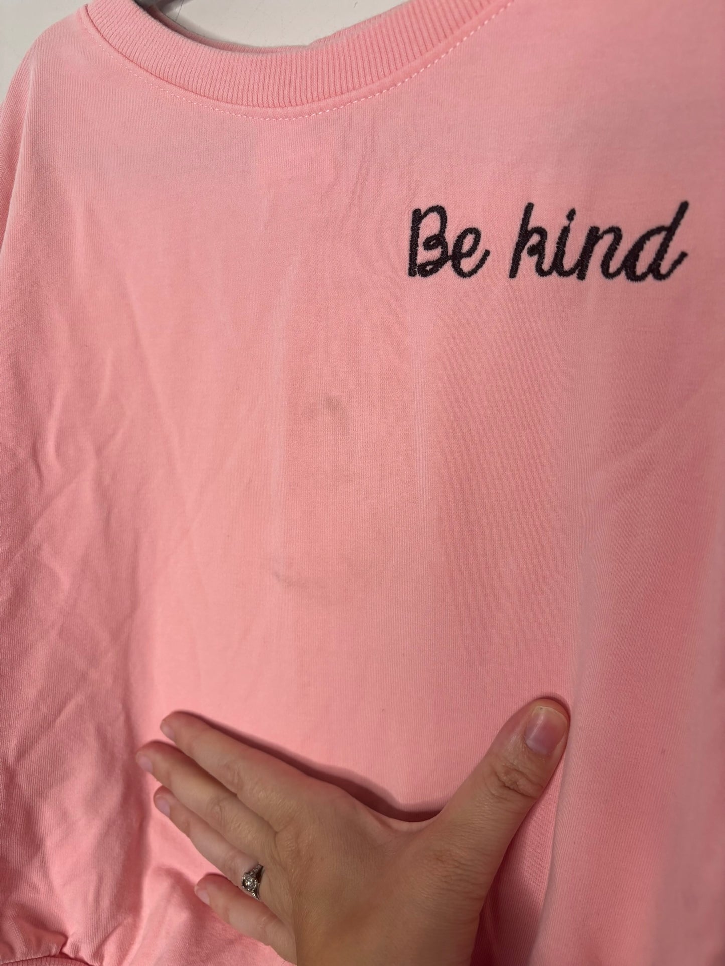 Pink baby onesie with 'Be kind' embroidered on the chest, featuring snap closures at the bottom.