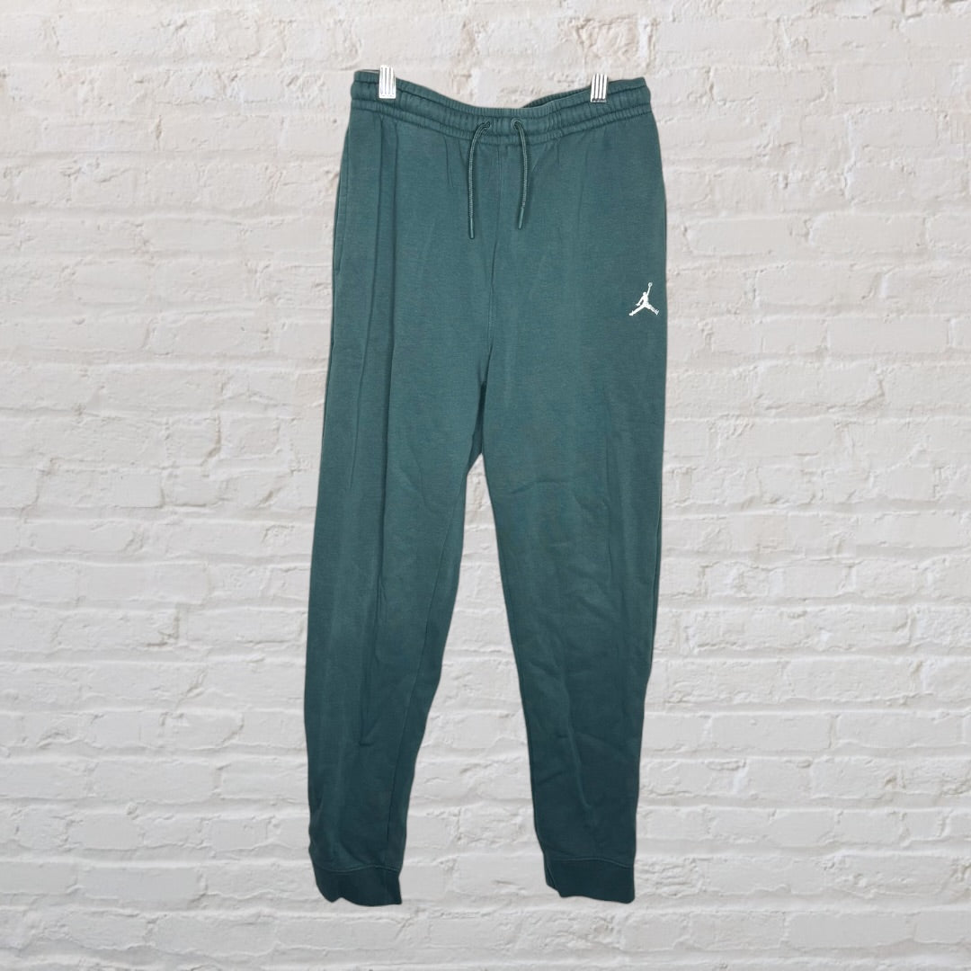 Dark teal Jordan athletic joggers hanging against a white brick wall, featuring the iconic Jumpman logo.