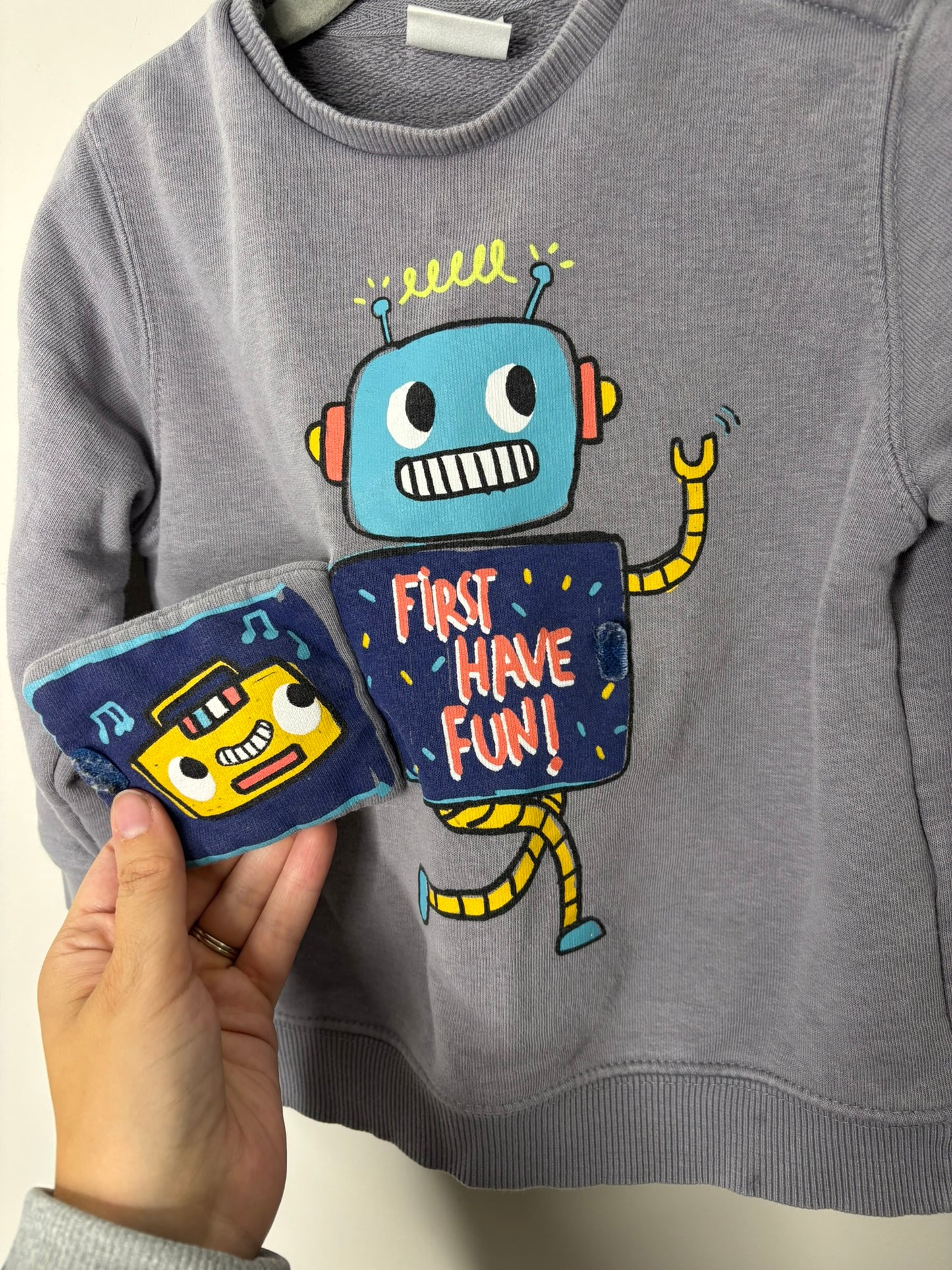 Grey sweatshirt featuring a colorful robot graphic on the front, hanging on a dark hanger.