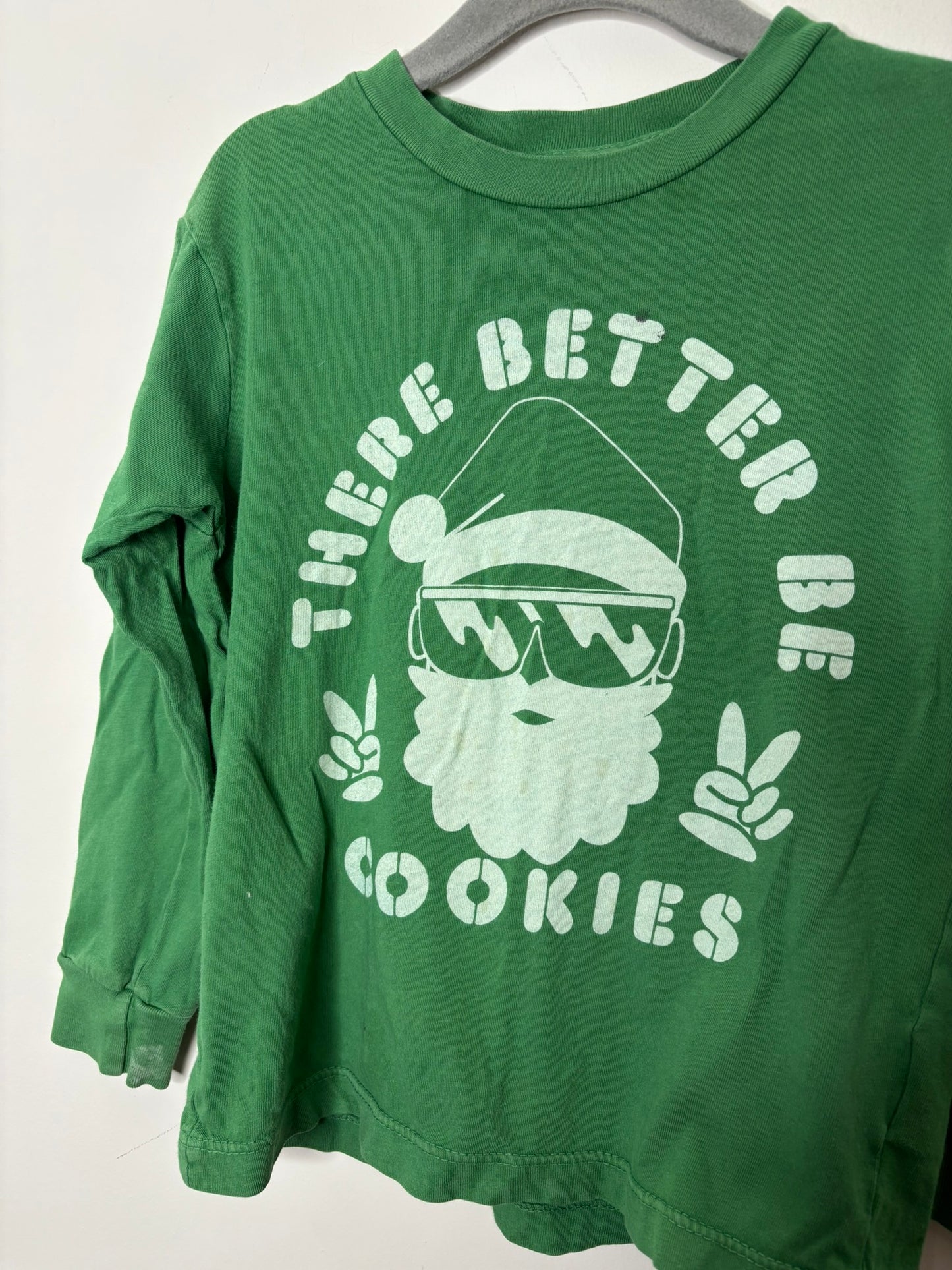Green long-sleeve T-shirt with a Santa graphic and 'There Better Be Cookies' text, hanging on a hanger.