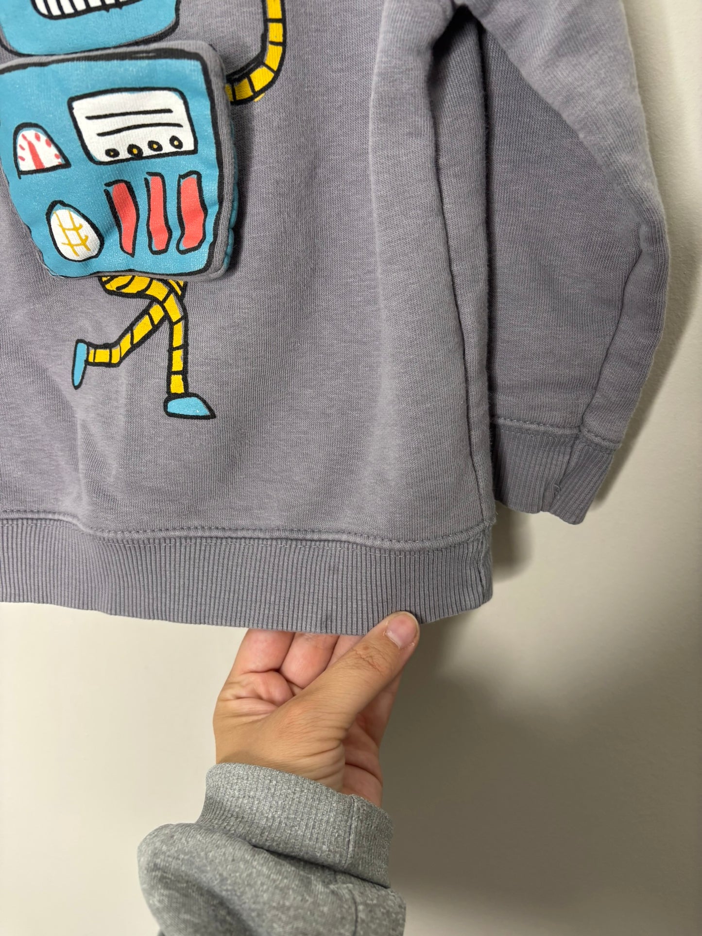 Grey sweatshirt featuring a colorful robot graphic on the front, hanging on a dark hanger.