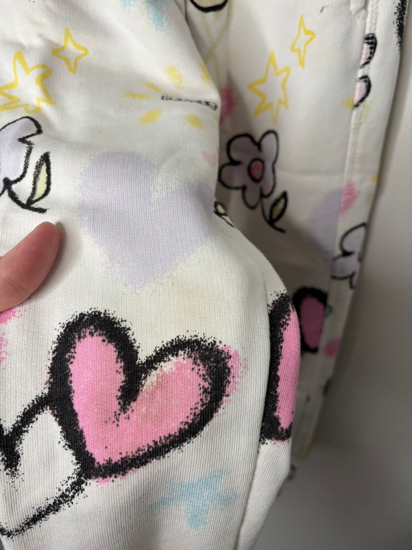 White sweatpants with colorful graphic prints of hearts, flowers, and stars.