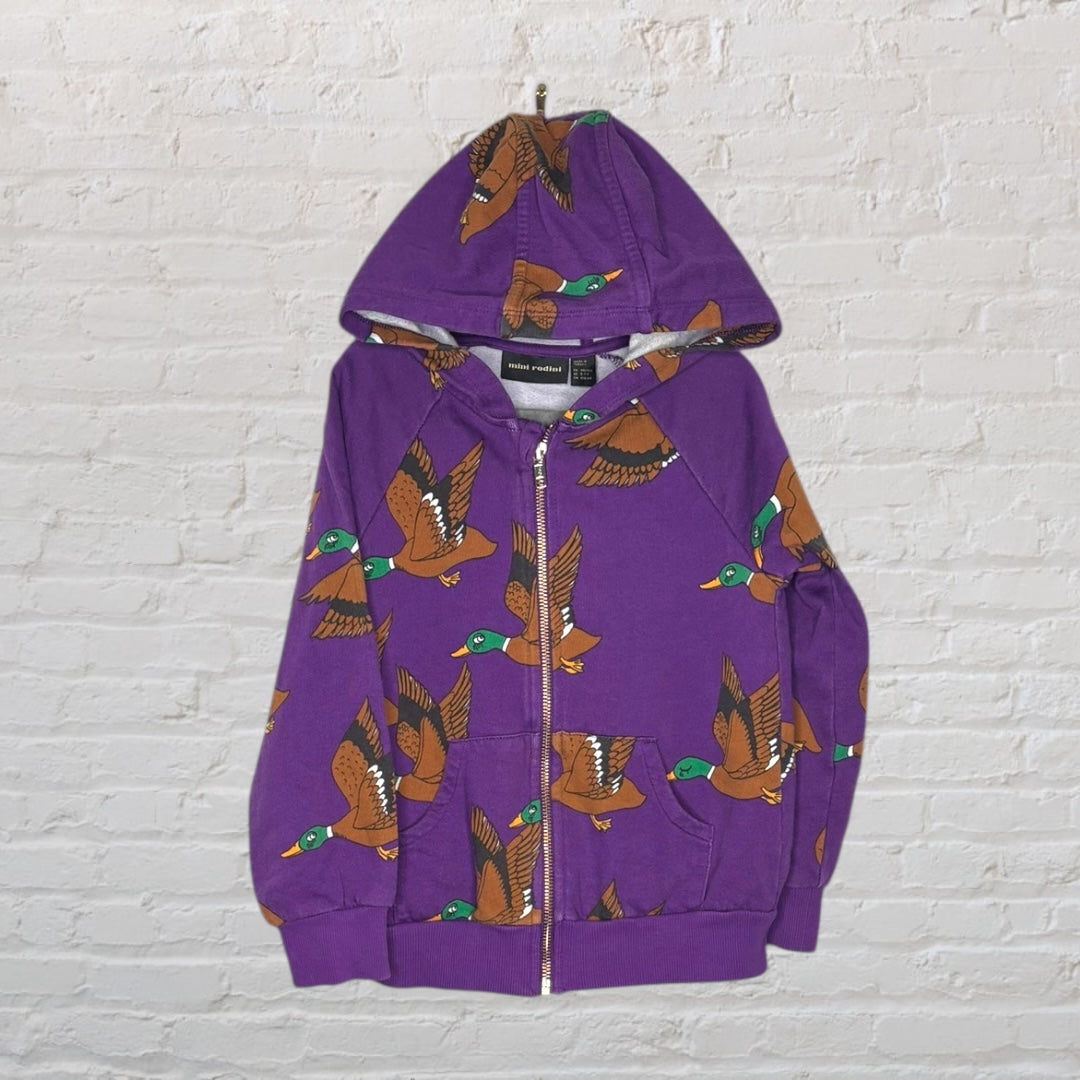 Purple zip-up hoodie with a brown duck print design by Mini Rodini, displayed against a white brick wall.