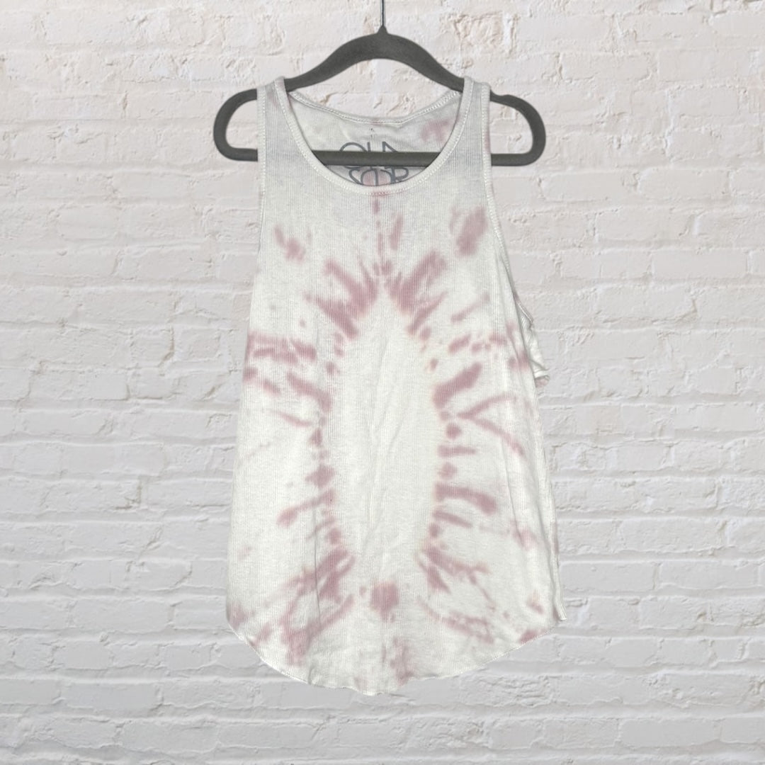 White and pink tie-dye tank top hanging on a black hanger against a brick wall.