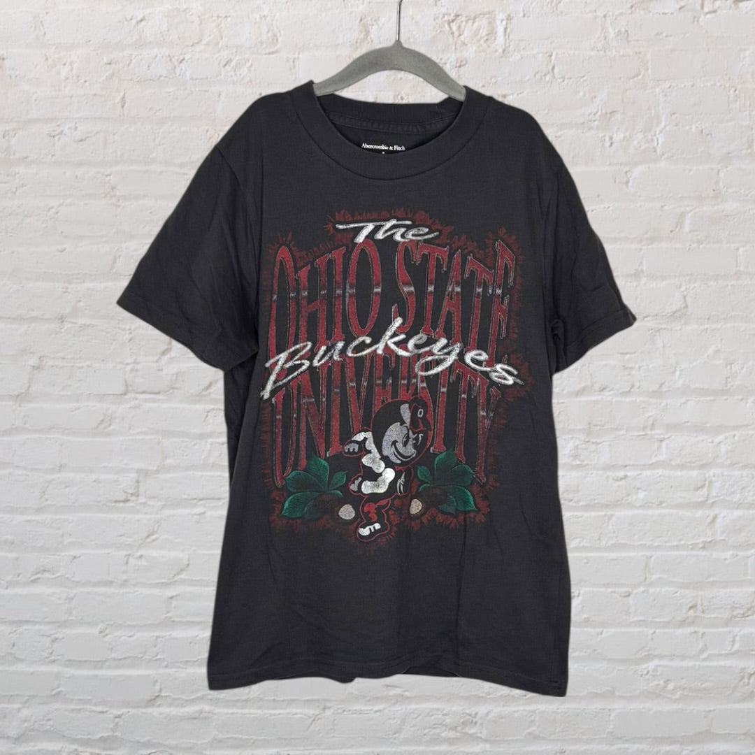 Black Ohio State Buckeyes T-shirt with large graphic and text on the front, hanging on a hanger.