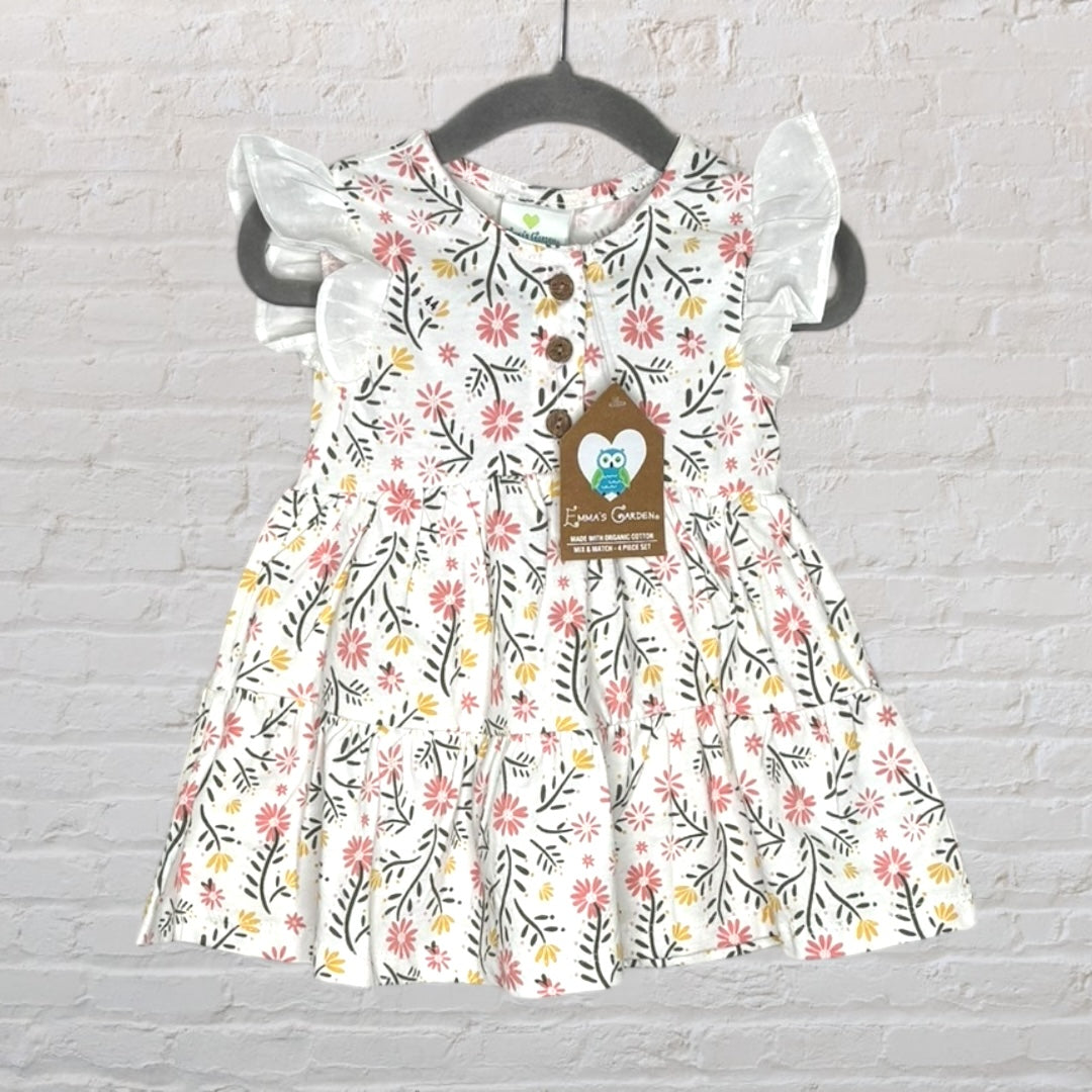 White dress with pink and yellow floral pattern, ruffle sleeves, and wooden buttons, tagged with 'Emma's Garden', hanging on a dark hanger.