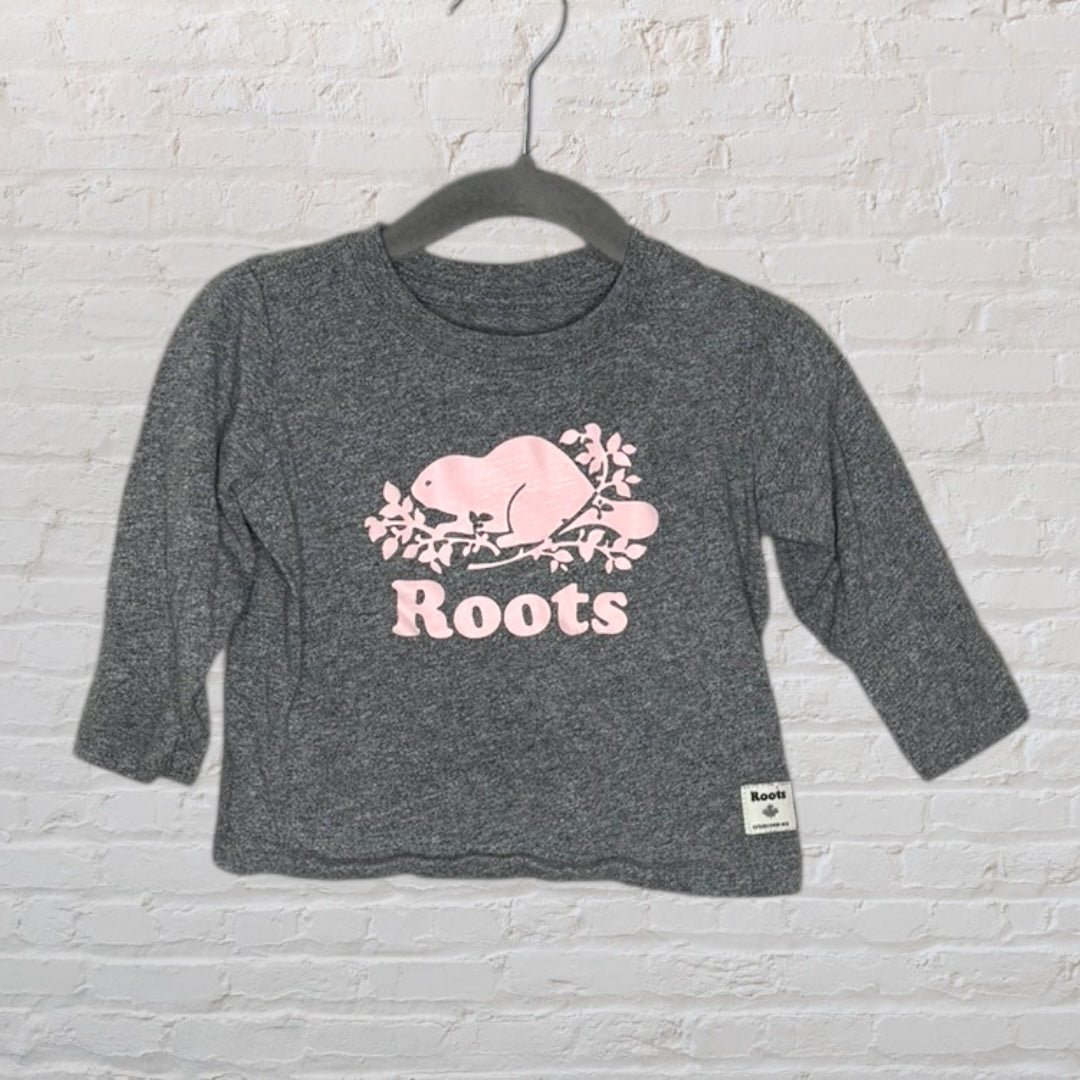 Grey long-sleeve t-shirt with pink Roots beaver logo, hanging on a hanger.