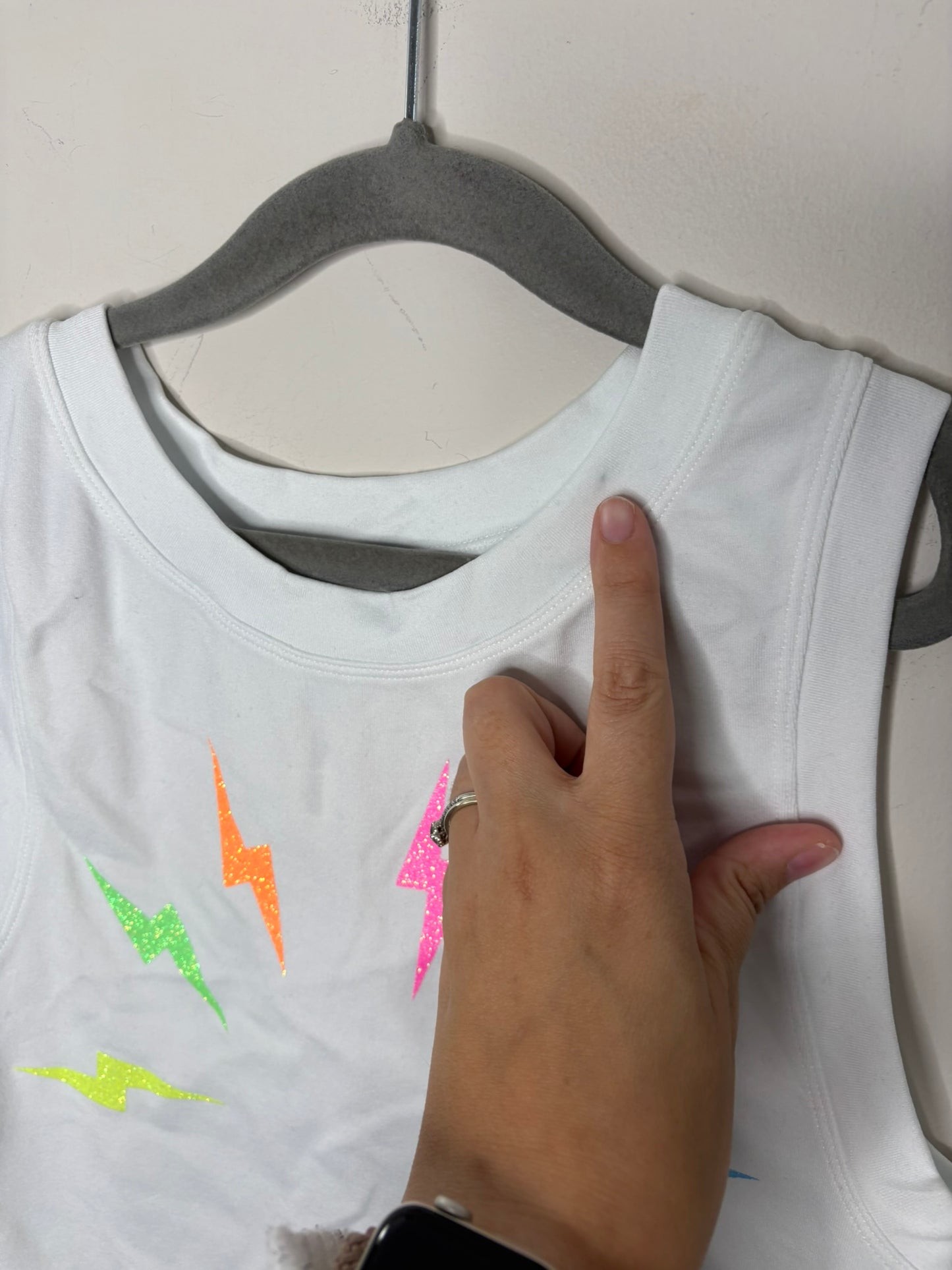 White tank top with colorful lightning bolt graphics and sleeveless design on a black hanger.