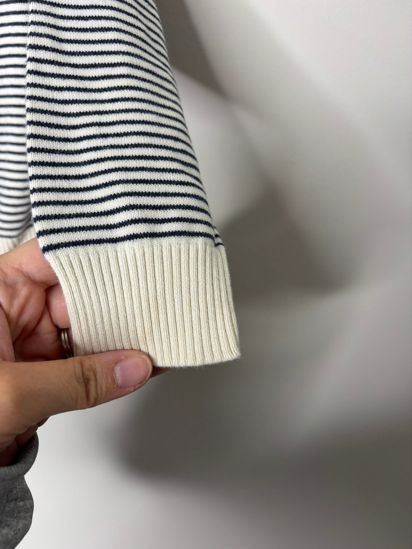 A black and white striped knit sweater with ribbed cuffs and neckline, hanging on a black hanger.