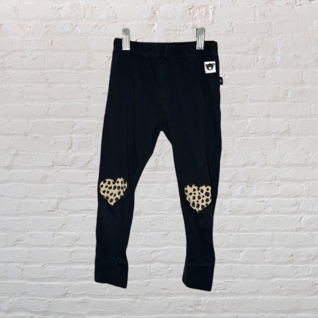 Black leggings with leopard print heart patches on the knees, hanging on a white textured background.