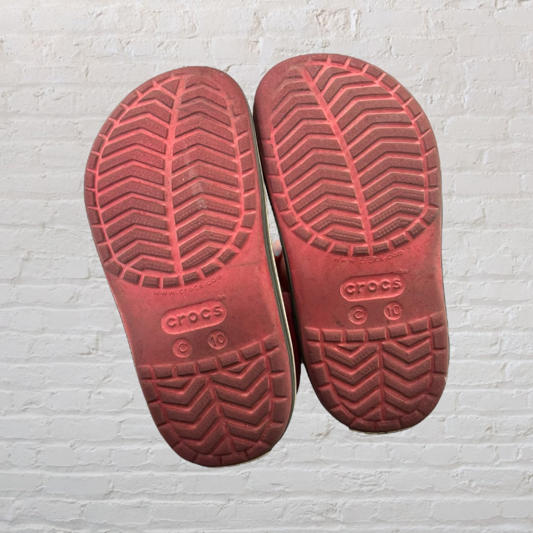 Pair of pink Crocs Classic Clogs with a white and black stripe on the sole, featuring ventilation holes and a strap.