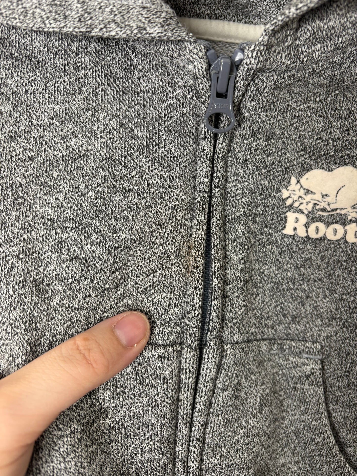 Grey Roots zip-up hoodie with logo on the chest, displayed on a hanger against a brick wall.