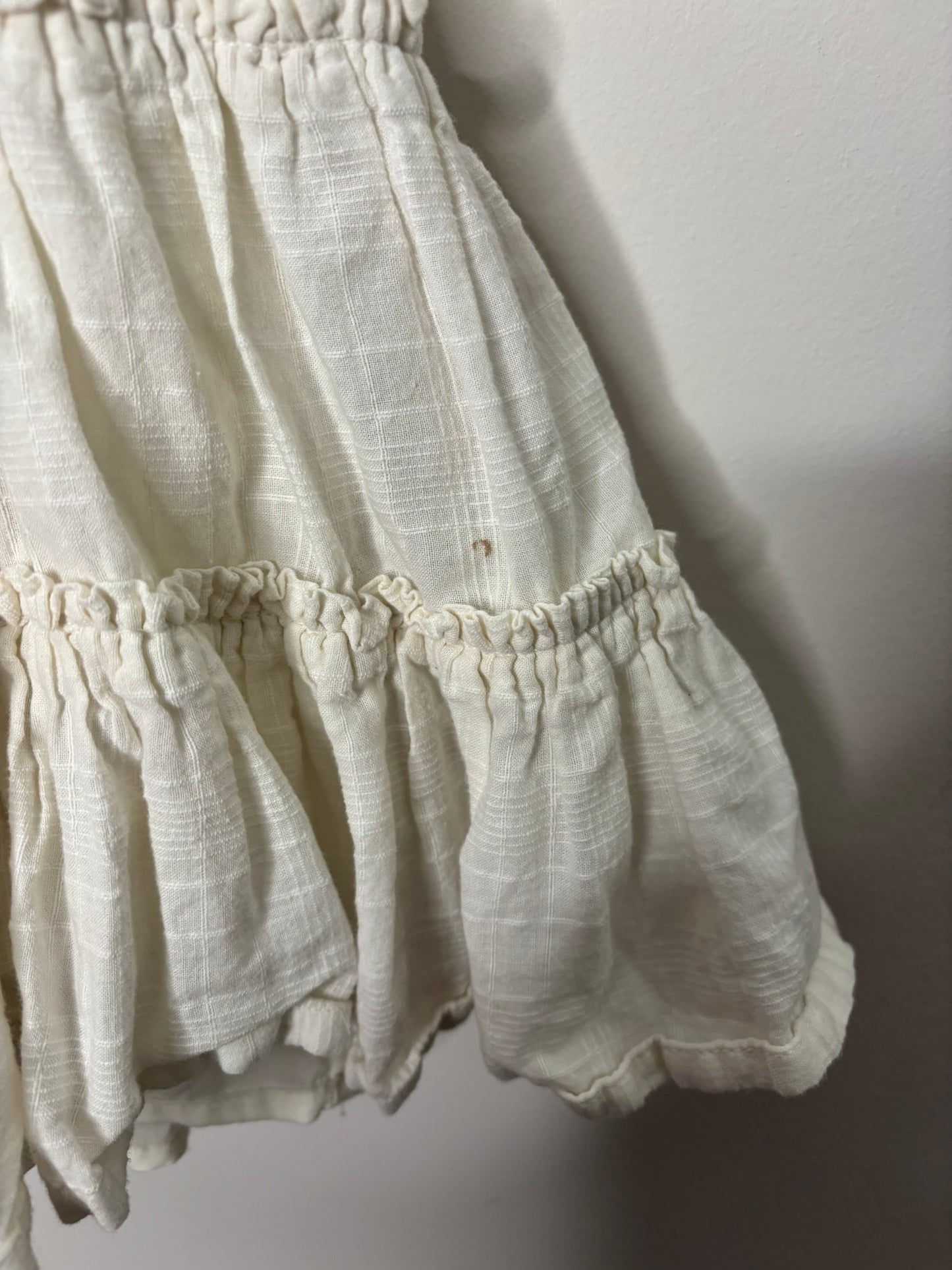Cream and peach sundress with crochet top and daisy embellishments, hanging on a black hanger.