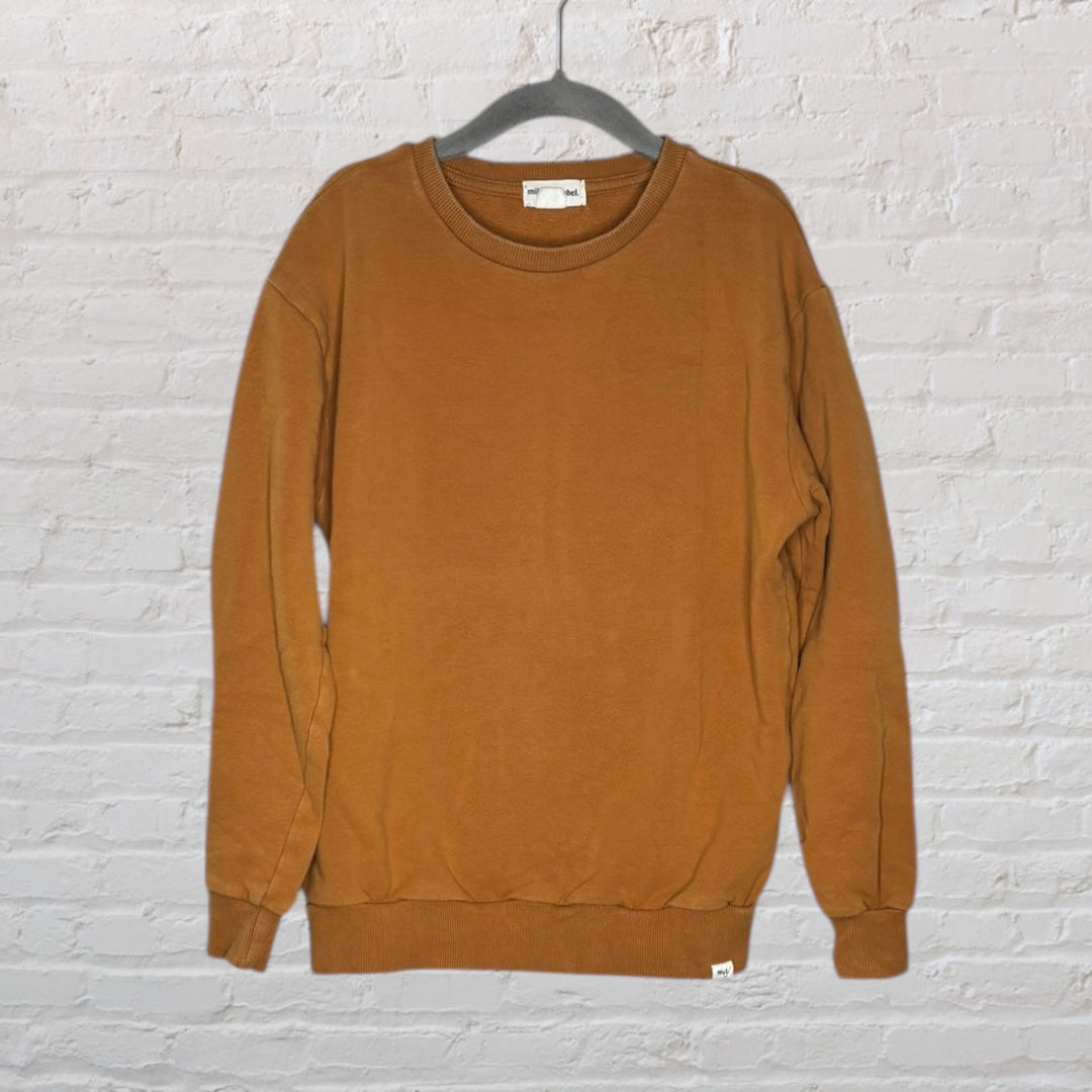 A plain brown crewneck sweatshirt hung on a hanger against a white brick wall.