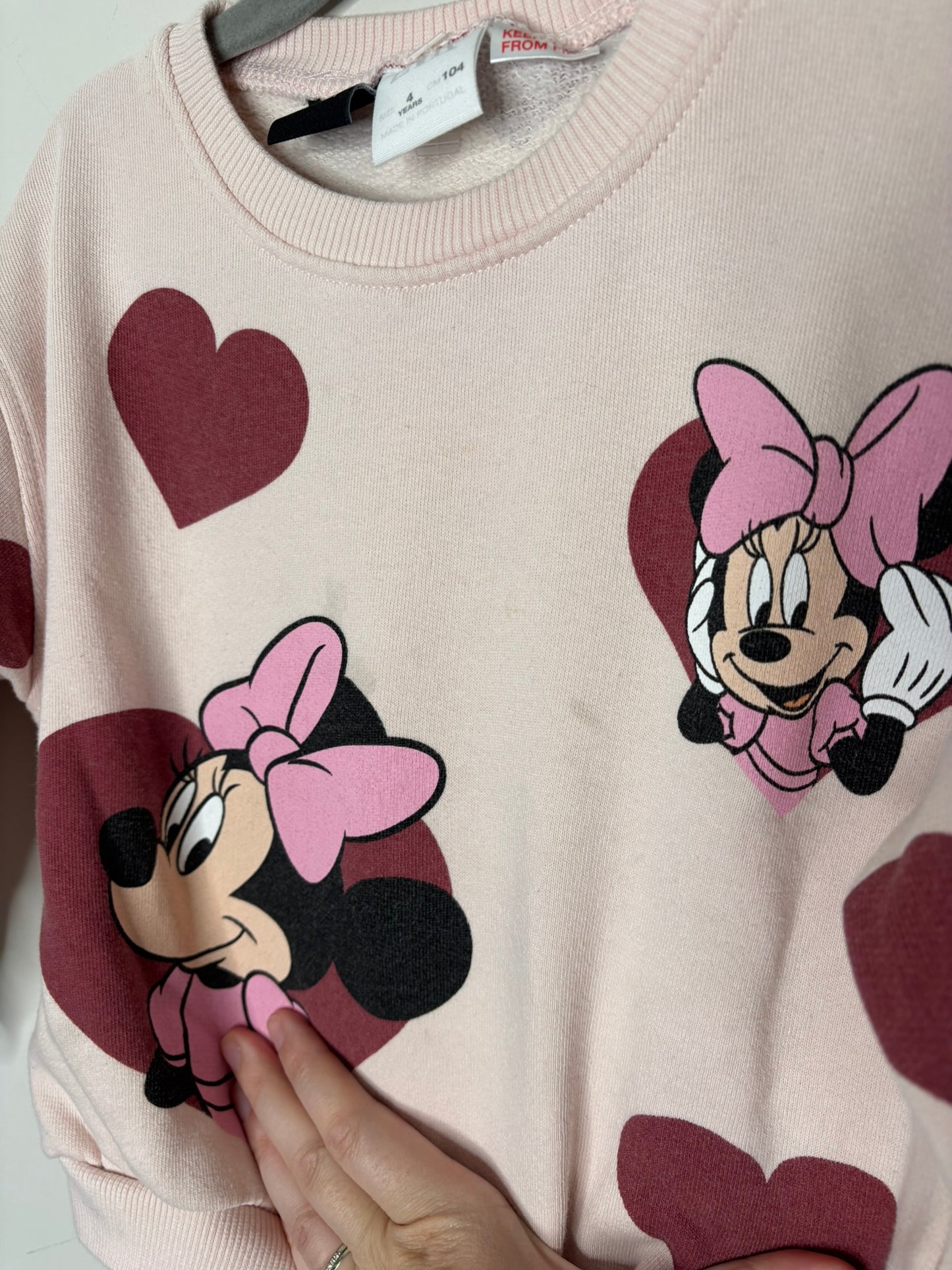 A pink sweatshirt featuring Minnie Mouse graphics and red heart patterns, displayed on a hanger.
