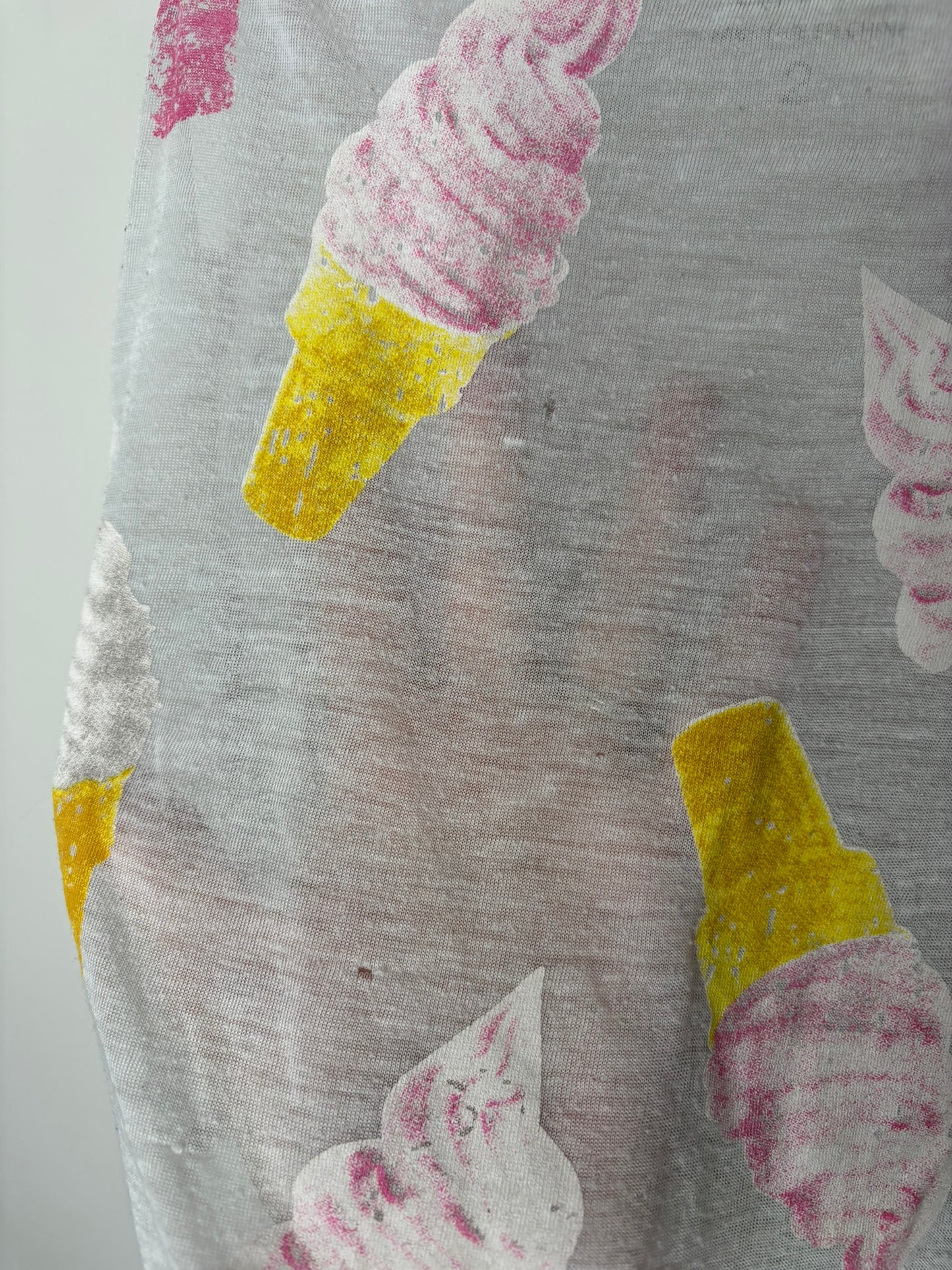 Sleeveless white top with colorful ice cream cone graphics in pink and yellow, hanging on a black hanger.
