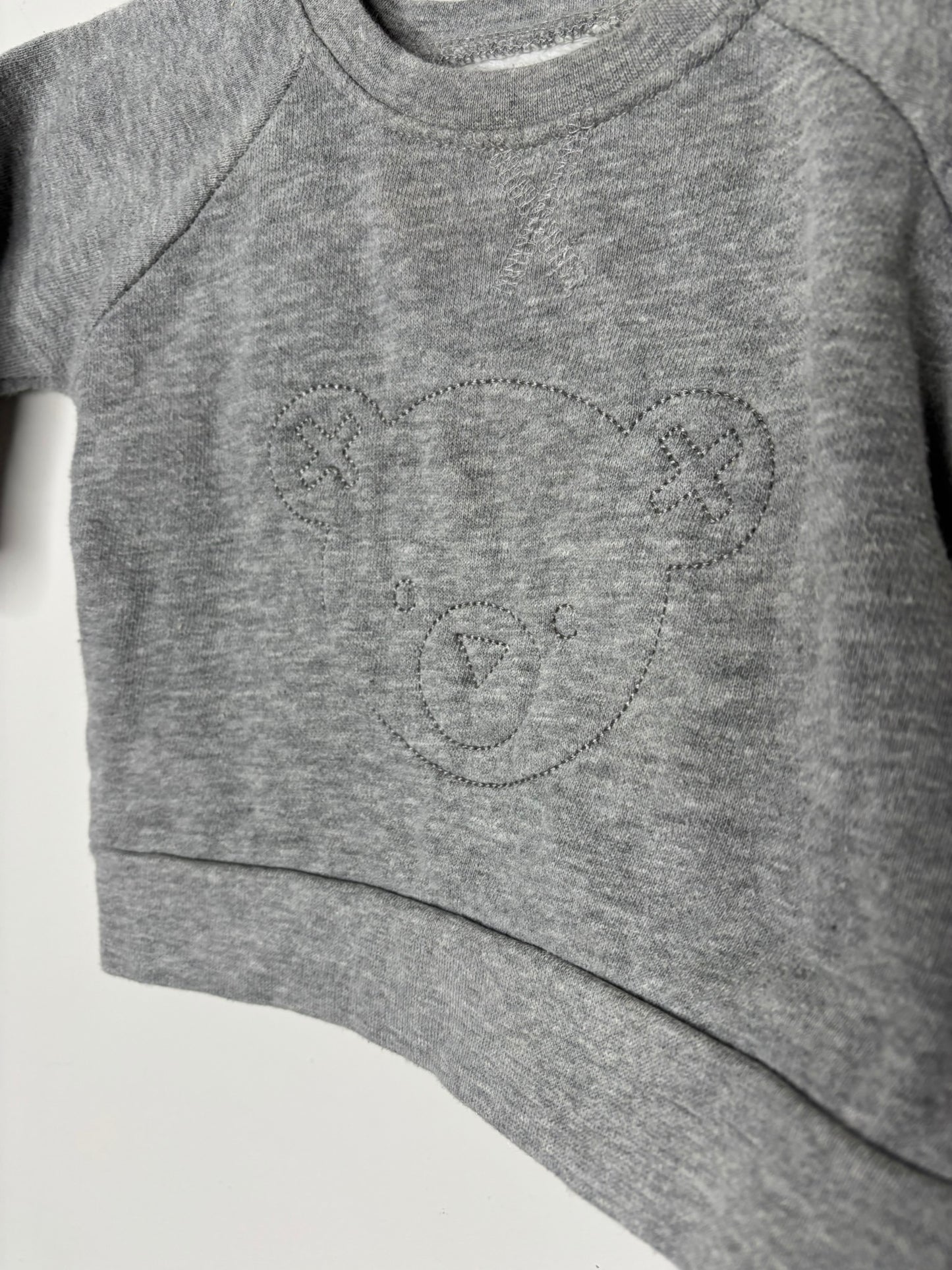Grey sweatshirt for kids with an embroidered bear design on the front, displayed on a hanger.