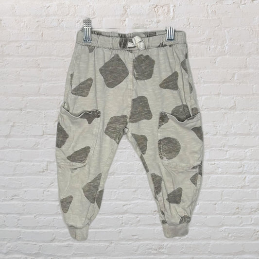 Olive and gray jogger pants with a camouflage pattern, displayed against a white brick background.