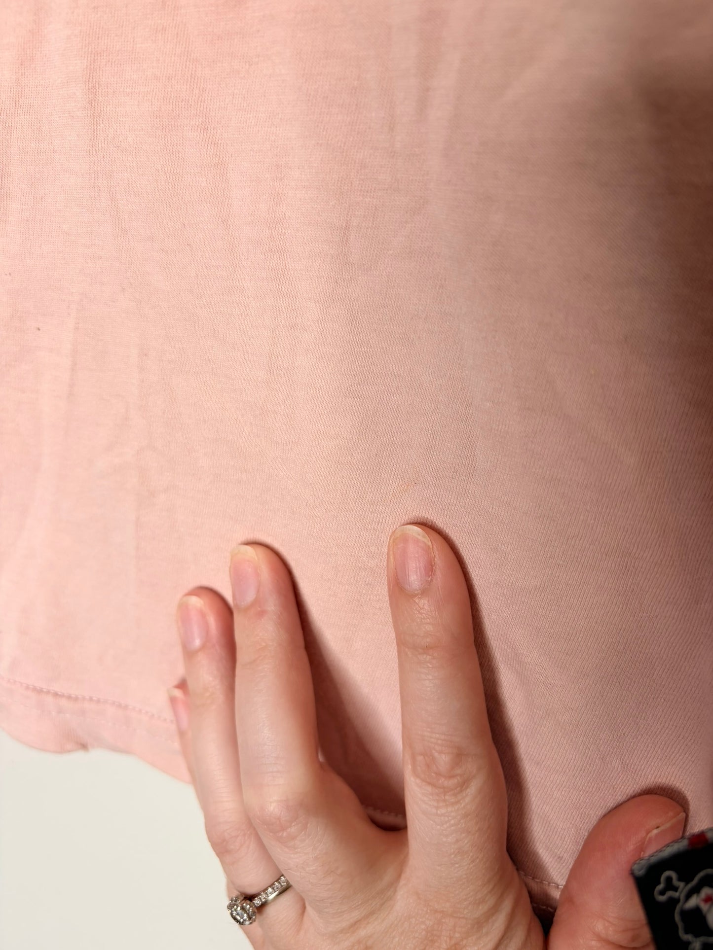 Pink short sleeve T-shirt with a large black and white eye graphic, layered over black long sleeves, hanging on a hanger.