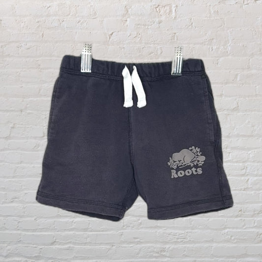 Black Roots shorts with white drawstring and logo on the leg, displayed against a brick wall.