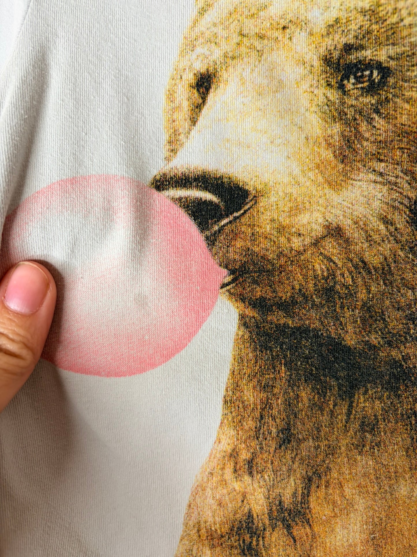 Off-white T-shirt featuring a graphic of a bear blowing pink bubblegum, hung on a hanger.