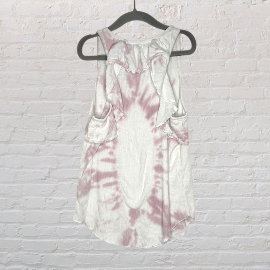 White and pink tie-dye tank top hanging on a black hanger against a brick wall.