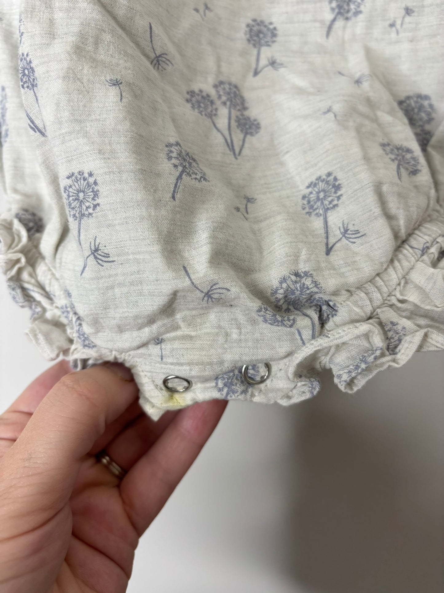 Light grey baby romper with purple floral print and ruffled sleeves, hanging on a black hanger.