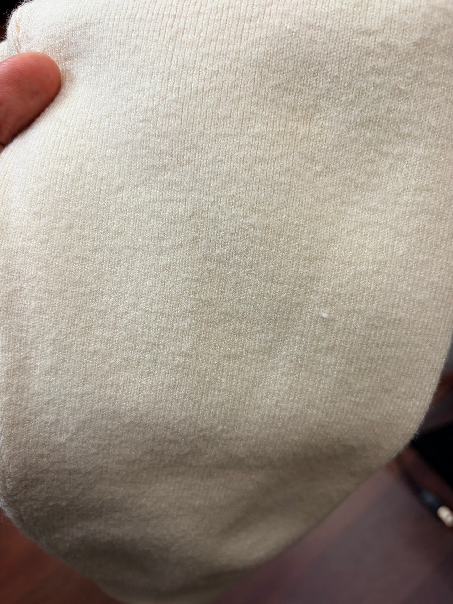 Cream-colored knit sweater and pants set hanging on a hanger against a white brick wall.