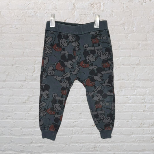 Dark grey joggers with Mickey Mouse print, featuring elastic waistband and cuffs.