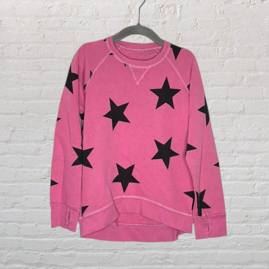 Pink sweatshirt with black star pattern, displayed on a hanger against a white brick wall.
