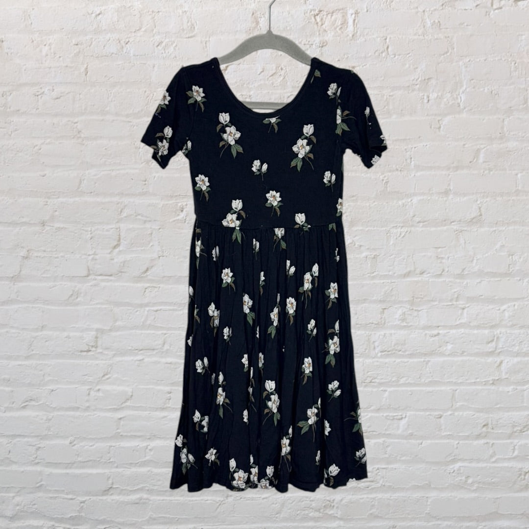 Black dress with white floral print and short sleeves, hanging against a white brick wall.